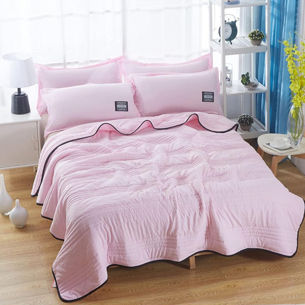 Quilted summer blanket draped over a bed with dark contrast edging