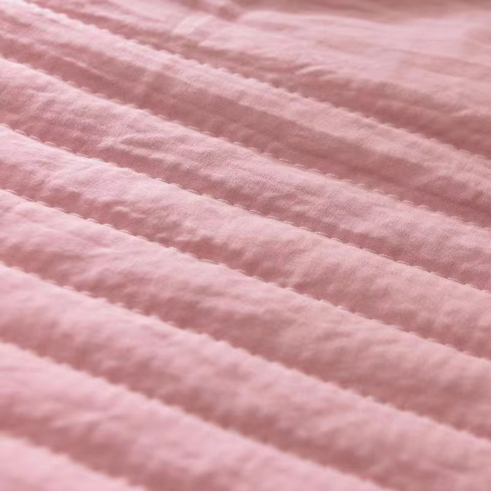 Quilted summer blanket draped over a bed with dark contrast edging