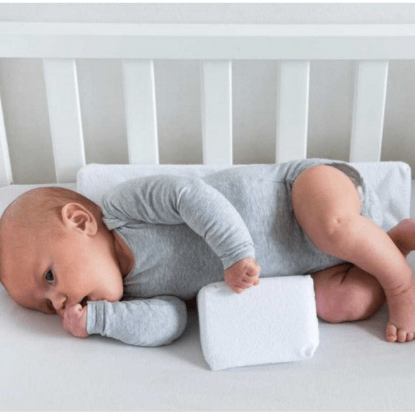 Baby positioning pillow with raised side supports in a cot