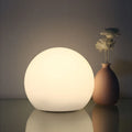 White spherical wireless LED table lamp glowing on a shelf