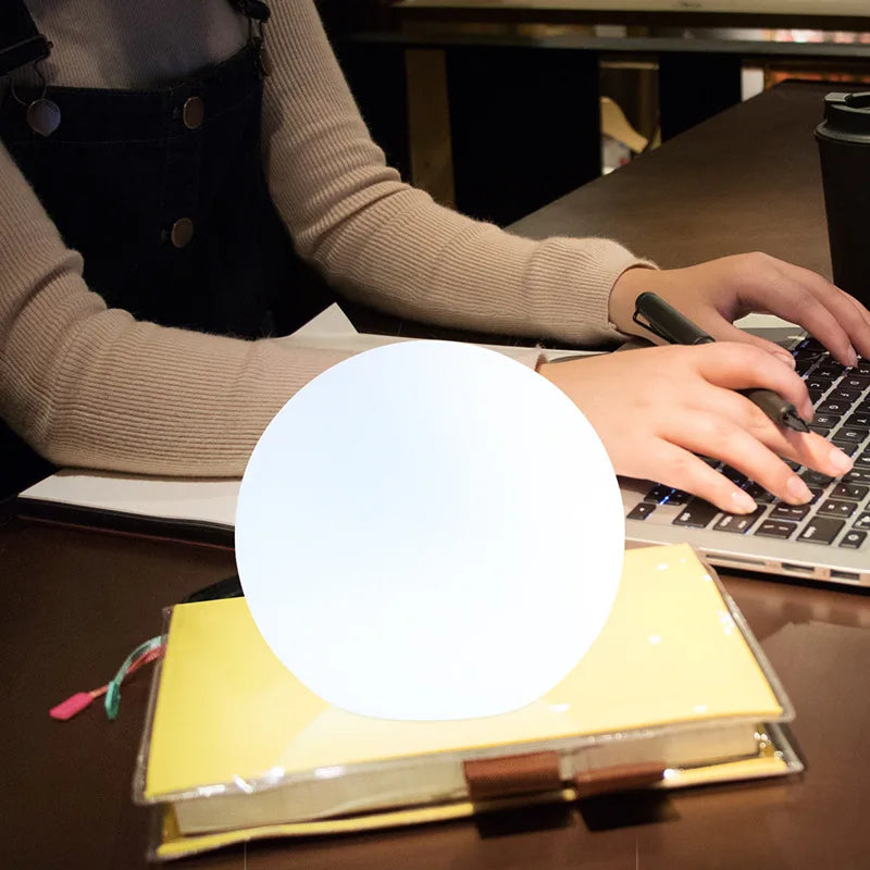 White spherical wireless LED table lamp glowing on a shelf