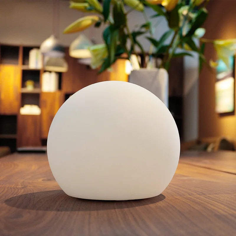 White spherical wireless LED table lamp glowing on a shelf