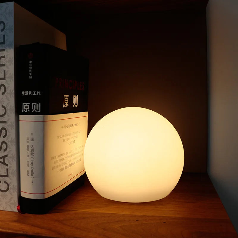 White spherical wireless LED table lamp glowing on a shelf