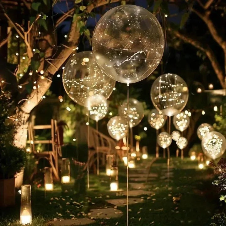 Clear balloons with warm white lights arranged along a garden path and event table