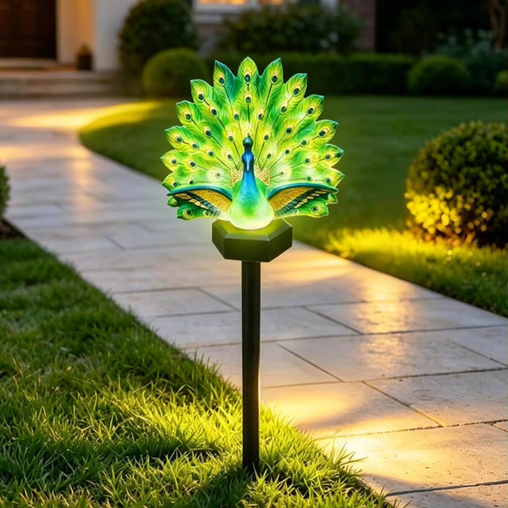 Illuminated peacock solar garden stake light in a planted border