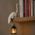 Cat figurine perched on a shelf with a hanging LED lantern
